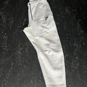 Nike tech byxor  - Helt Nya . Snygga vita mjukisbyxor från Nike med svart logga på låret, elastisk midja med snörning och svarta dragkedjor vid fickorna. Sköna och stilrena byxor i mjukt material, perfekta för chill eller träning. M passar även S , skriv för mer info ! 