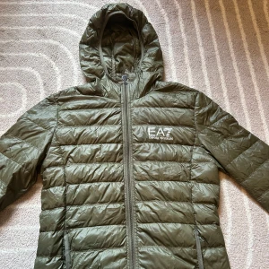 Grön pufferjacka från Emporio Armani - Säljer en EA7 Emporio Armani jacka i nyskick – aldrig använd, bara provad. Jackan är 100% äkta och köpt från officiell återförsäljare  🖤 Färg: Mörkgrön 📏 Storlek:S 🎯 Passform:normal 🧵 Material:   🔥 Nypris: ca [2499] 💸 Mitt pris: 549kr !  ✔️ Inga defekter ✔️ Röker ej ✔️ Inga husdjur  📦 Skickas snabbt 📩 Fråga gärna om fler bilder 