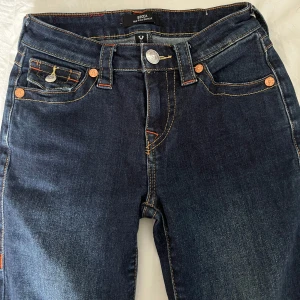 True Religion mörkblå bootcut jeans - Säljer mina mörkblå jeans från True Religion med bootcut passform och snygga kontrastsömmar. Klassiska fickor med lock och silverknappar bak Jeansen har låg midja. Har sytt up dom satt dom passar mig som är 160cm lång. Pris kan diskuteras vid snabb affär 