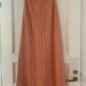Lång stickad kjol i persikorosa - Superfin långkjol i persikorosa stickat material med diskreta ränder. Kjolen har en mjuk innerskjol Längd: 100 cm midja: 72. Den sitter lite tajt runt min midja och jag är storlek M. Den sitter hög midjat 
