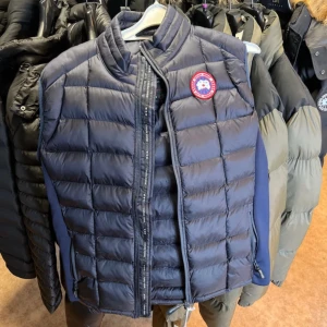 Mörkblå dunväst från Canada Goose - Säljer en mörkblå quiltad dunväst från Canada Goose, modell Hybridge Lite Tech Vest. Västen har hög krage, dragkedja framtill och klassisk logotyp på bröstet. Tillverkad i lätt och smidig polyester med dunfyllning. Perfekt lager-på-lager-plagg för kyliga dagar.