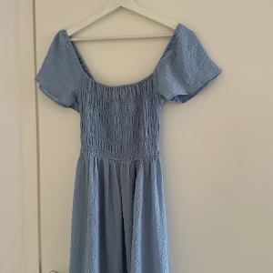 Ljusblå långklänning med puffärm - Superfin ljusblå långklänning med smockad överdel och vida puffärmar. Klänningen har en  kjol med volang nertill. Storlek 34 men passar nästan bättre på 36. Använd en gång🩵