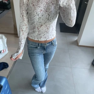 Vit spetsblus från Gina Tricot - Supersnygg vit långärmad blus i spets från Gina Tricot. Blusen har blommigt spetsmönster, är figurnära och croppad i modellen. Perfekt att styla med jeans eller kjol för en trendig look.