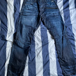 Mörkblå jeans från Jack & Jones - Säljer ett par mörkblå jeans från Jack & Jones med coola sömdetaljer och dragkedja vid fickan. Jeansen har en snygg tvättad look och raka ben. Perfekta för dig som gillar en avslappnad men ändå stilren vibe.