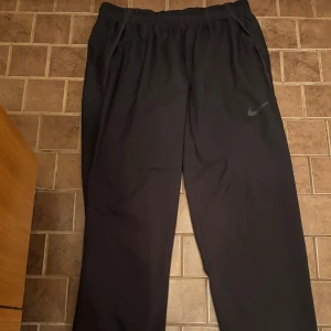 Svarta träningsbyxor från Nike - Svarta träningsbyxor från Nike med elastisk midja och dragsko. Byxorna har en loose passform och är tillverkade i ett lätt syntetmaterial. Swoosh-loggan syns diskret på ena benet. Perfekta för chill eller sportiga dagar. Väldigt bra skick och endast använda ett fåtal gånger! Väljer du att betala direkt via Swish kan jag gå ner lite i pris eftersom vi då slipper all väntetid som tillkommer via betalning genom Plick!🏆 Skicka ett PM vid frågor eller funderingar.
