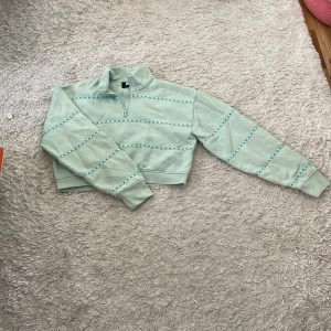 Mintgrön fleece half zip från ME. - Supermjuk mintgrön fleece-tröja från ME. med croppad passform och halv dragkedja. Dekorativa band med ME.-logga i samma färg går tvärs över bröstet och ärmarna. Perfekt för lager-på-lager och chill dagar.