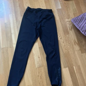 Svarta leggings från Iconic, stl M - Svarta leggings från Iconic i stretchigt material, perfekt för träning. Hög midja och tight passform. Snyggt tryck med 'ICONIC' längs benet och diskret logga vid höften. Supersköna och följsamma för alla dina aktiva dagar.