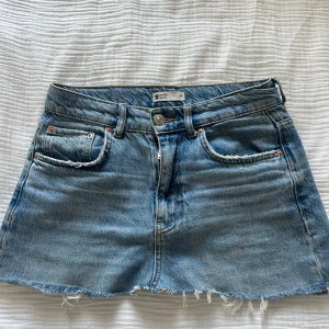 Blå jeanskjol från Perfect Jeans - Snygg blå jeanskjol från Perfect Jeans med rå kant nertill och klassiska fem fickor. Kjolen har bälteshällor, knapp och dragkedja framtill samt cool slitning vid fickorna. Perfekt för en chill och trendig look.