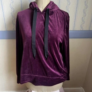 Mörklila sammetshoodie - Mysig hoodie i mörklila sammet från Esmara. Tröjan har huva med breda svarta snören och lång ärm. Väldigt mjukt material och sparsamt material 🩷 Lite liten i storleken