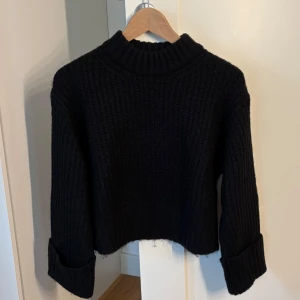 Svart stickad croppad tröja - Mysig svart stickad tröja med croppad passform och breda uppvikta ärmar. Tröjan har aldrig kommit till användning, endast prislappen är av. 