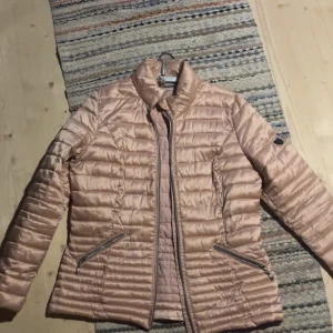 rosa pufferjacka från Isolde, stl 38 - Snygg rosa pufferjacka från Isolde i storlek 38. Den är mer rosa i verkligheten, Jackan har glansig yta, horisontella sömmar och två dragkedjefickor framtill. Perfekt för dig som vill ha en lätt och trendig jacka med stilren look.