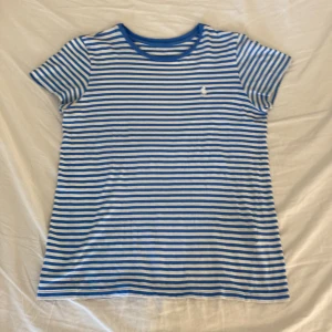 Randig t-shirt från Ralph Lauren - Blåvit randig t-shirt från Ralph Lauren med klassisk broderad logga på bröstet. T-shirten har rund halsringning och korta ärmar. Skön passform och tillverkad i mjuk bomull, perfekt för en chill look.storlek S-M💙🤍