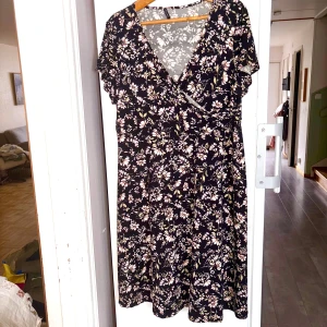 Svart blommig klänning - Supersöt svart kortklänning med rosa och vita blommor,, avsluten vid bysten och v-ringning. Klänningen har korta ärmar och ett flowy fall som ger en avslappnad men ändå feminin vibe. 