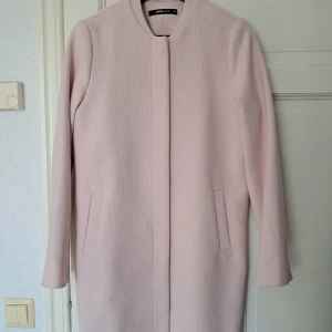 Ljusrosa kappa från Gina Tricot - Säljer en stilren ljusrosa kappa från Gina Tricot i storlek 34. Jackan har rak passform, diskreta fickor och knäpps med dolda knappar framtill. Materialet är strukturerat och fodret är slätt, perfekt för vår och höst. Bomull