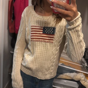 Beige stickad tröja Ralph Lauren - Snygg beige kabelstickad tröja från Ralph Lauren med amerikansk flagga broderad framtill. är i storlek M men passar mig som normaltsätt har xs/s i storlek. tröjan är knappt använd och säljer därför den💕