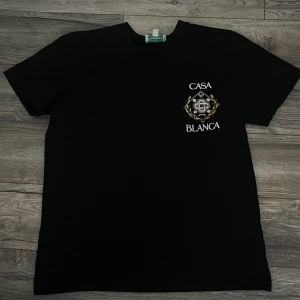 Svart Casablanca t-shirt med tryck - Svart t-shirt från Casablanca med stort färgglatt emblem och texten 'Casa Blanca' på både bröstet och ryggen. Klassisk passform och korta ärmar, tillverkad i mjuk bomull. Perfekt för dig som gillar streetwear med exklusiv vibe.