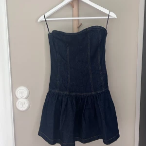 Mörkblå jeansklänning från Gina Tricot - Supersöt mörkblå jeansklänning från Gina Tricot med  volang nertill. Klänningen är kort och har en figurnära passform som framhäver midjan. Perfekt för dig som vill ha en trendig och stilren look i denim.  Pris kan diskuteras 
