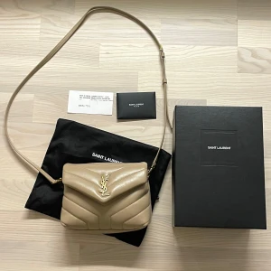 Ysl Lou Lou toy - Ysl väska i Lou Lou toy modell, beige med guld detaljer. Väskan är i nyskick och har använda fåtal gånger. Jag köpte väskan på Vinted där jag fick bifogat ett kvitto som jag skickar bild på vid köp. Dustbag, box och mini kuvert medföljer.