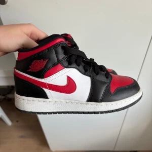 Nike Air Jordan 1 Mid Svart/Röd/Vit - Snygga Nike Air Jordan 1 Mid sneakers i svart, rött och vitt skinn. Knappt använda. 