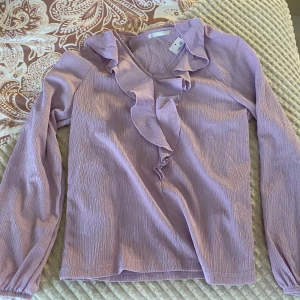 Ljuslila blus med volangdetalj - Supersöt ljuslila blus från Ellos med volang längs v-ringningen. Långärmad modell i lätt, krinklat tyg. Perfekt att styla med jeans eller kjol. 🩷🩷kan tänka mig sänk pris vid snabb affär 