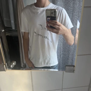 Vit Saint Laurent t-shirt - Vit t-shirt från Saint Laurent med svart handskriven logga på bröstet. Klassisk rund halsringning och korta ärmar. Tillverkad i mjuk bomull för en skön och avslappnad känsla. Perfekt för en clean och stilren look. Skriv för fler bilder och kom gärna med prisförslag 