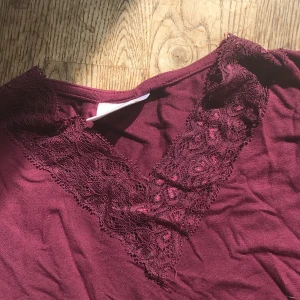 Vinröd spetsdetaljerad topp Gina Tricot - Vinröd långärmad topp från Gina Tricot med v-ringning och snygga spetsdetaljer runt halsen. Mjuk och skön, perfekt för dig som gillar en feminin touch. Passar till jeans eller kjol för en chill men ändå stilsäker look.