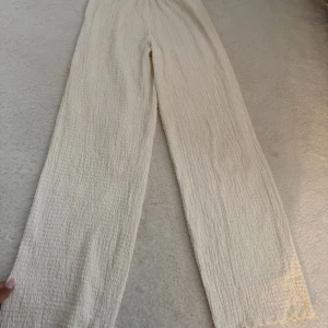Beiga vida byxor med struktur - Säljer ett par beiga byxor med snygg struktur och relaxed fit. Byxorna har resår i midjan och raka, vida ben. Perfekta för en chill och stilren look. Materialet är luftigt och passar grymt till varmare dagar.