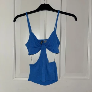Blå linnetopp från H&M Divided - Säljer en snygg blå linnetopp från H&M Divided med smala axelband och snygg knutdetalj framtill. Toppen har öppen rygg och coola cut-outs både fram och bak, vilket ger en trendig look. Tidigare klippt lite kortare pågrund av att den var för lång. 