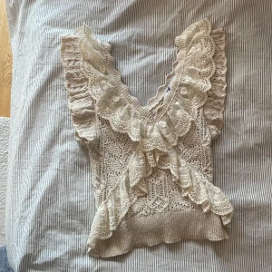 Beige spetsblus med volang från Zara - Superfin beige blus från Zara med virkade detaljer och breda spetsvolanger längs v-ringningen och axlarna. Ärmlös modell med romantisk känsla och ribbad nederkant. Perfekt för dig som gillar en söt och bohemisk stil.