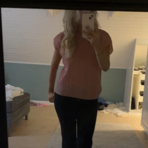 Rosa plisserad blus med kort ärm - Säljer en ljusrosa blus med plisserat tyg och korta ärmar. Toppen har en rak passform och rund halsringning. Perfekt för dig som gillar en enkel men ändå trendig look. Materialet känns lätt och luftigt, vilket gör den skön att bära.