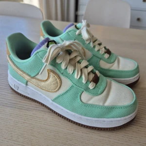 Nike Air Force 1 '07 LX - 'Happy Pineapple'  - Unika Nike Air Force 1 '07 LX "Happy Pineapple" i mintgrönt och beige/gul med detaljer i ljusbrunt och lila. Ovandel i canvas och mocka, vit sula med brun undersida. Klassisk snörning och broderad ananaslogga på plösen. Perfekta för dig som vill sticka ut med stilrena färger. Endast använd vid tre tillfällen, så skorna är som i nyskick! Nypris 2695 kr. 
