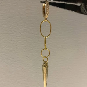 Guldigt örhänge med kedja och kon - Coolt örhänge i guld med kedjelänkar och en spetsig konformad detalj längst ner. Örhänget har en liten ring upptill med glittriga stenar och hänger snyggt i örat. Perfekt för dig som gillar statement-smycken.