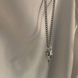Silverfärgat halsband med fågelkranium - Unikt halsband i silverfärg med en kedja och ett detaljerat hänge som liknar ett fågelkranium. Perfekt accessoar för dig som gillar edgy och annorlunda smycken. Kedjan är grov och hänget har en cool, rå känsla.