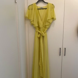 Ljusgul långklänning  - Superfin ljusgul långklänning med v-ringning, volangärmar och knytband i midjan. Klänningen har ett luftigt och flowy fall, perfekt för sommarens alla tillfällen. Materialet är lätt och känns riktigt skönt mot huden. Oklart med storleken men jag var mellan en L och Xl när jag hade den.