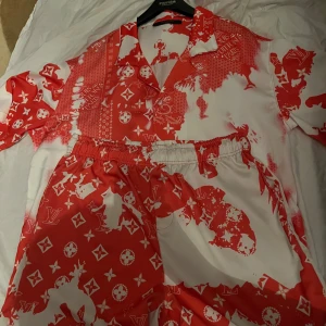 Louis Vuitton röda och vita shorts - Snygga shorts från Louis Vuitton i rött och vitt med ikoniskt LV-mönster och elastisk midja med snörning. De har en loose fit och är perfekta för sommaren. Materialet känns lätt och svalt, perfekt för varma dagar.