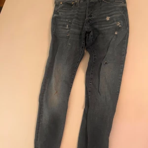 Blå slitna jeans från Jack & Jones - Säljer ett par blå jeans från Jack & Jones med slitningar och hål  vibe. Jeansen har klassisk femficksdesign, normal passform och är tillverkade i bomull. Perfekta.