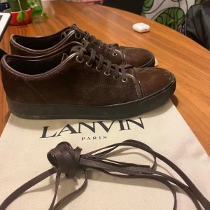 Bruna sneakers från Lanvin i mocka - Snygga bruna sneakers från Lanvin med ovandel i mocka och tåparti i blankt skinn. Skorna har svarta sulor och matchande bruna skosnören. Perfekta för dig som gillar stilrena och exklusiva sneakers med en lyxig känsla. Storlek 40-41