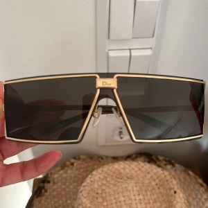Dior solglasögon med guldiga detaljer vintage 2000-tal - Snygga Dior solglasögon med rektangulär, oversized sköldform och guldiga metallbågar. Glasen är mörka och ger en futuristisk vibe. Dior-logga syns på både front och skalmar. Perfekta för dig som vill sticka ut med en lyxig accessoar. Inköpta 2001. 