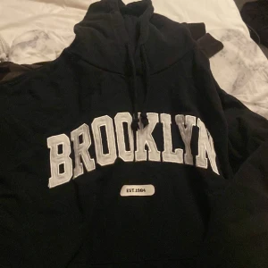 Svart hoodie med BROOKLYN-tryck - Svart hoodie med stor vit BROOKLYN-text framtill och snörning i luvan
