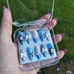 Blå och silver press-on naglar med stjärnor - Säljer handgjort sett press-on naglar i blått, silver och nude med coola svarta stjärnor, vita 3D-rosetter och pärldekor. Storleken är xs/s med måtten: 13, 11, 12, 11-12, 9 (mm). Lim ingår ej😊