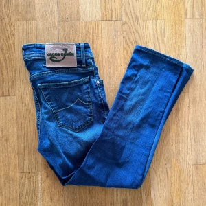 Blå jeans från Jacob Cohën - Snygga blå jeans från Jacob Cohën med klassisk femficksdesign, gröna detaljer och logotyp på bakfickan. Jeansen har en normal passform och är tillverkade i mjukt denimtyg med knappgylf och stilren look.