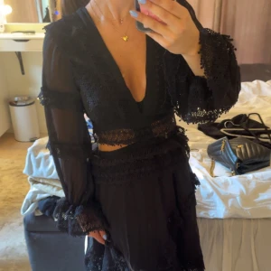 Svart omlottklänning med spetsdetaljer från raglady  - Supersnygg svart kortklänning från LPA med djup v-ringning, transparenta långärmar och spetsdetaljer. Klänningen har omlottkänsla, markerad midja och volang vid ärmslut och kjol. Perfekt för dig som vill sticka ut med en unik och trendig look. Aldrig använd, köpt på Raglady🫶🏼