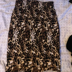 Leopardmönstrad långkjol - Snygg långkjol med leopardmönster i bruna, svarta och beige toner. Kjolen har en rak passform och är perfekt för dig som vill sticka ut med ett djuriskt print. Materialet känns mjukt och följsamt mot kroppen.