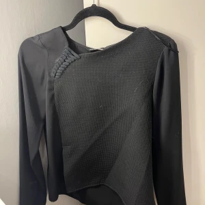 Svart asymmetrisk tröja från Zara - Svart långärmad tröja från Zara med cool asymmetrisk design och strukturerad framsida. Snygg detalj med flätad kant vid axeln och slät baksida. Perfekt för dig som gillar unika plagg med edge.