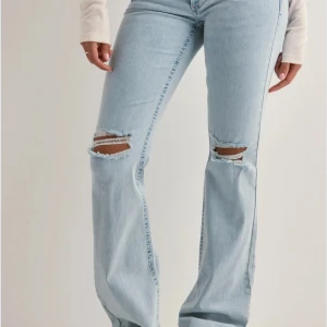 Ljusblå bootcut jeans från Nelly  - Snygga ljusblå jeans med bootcut passform och slitna hål på knäna. Jeansen har klassisk femficksdesign och coola rosa broderade detaljer på bakfickorna. Populära jeans som går att matcha med många toppar