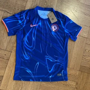 Chelsea FC blå matchtröja Nike S - Chelsea FCs officiella matchtröja från Nike i intensiv blå färg med unikt abstrakt mönster. Kortärmad modell med klubbmärke och Nike-logga på bröstet. Tillverkad i lätt och ventilerande Dri-FIT-material för maximal komfort på planen.