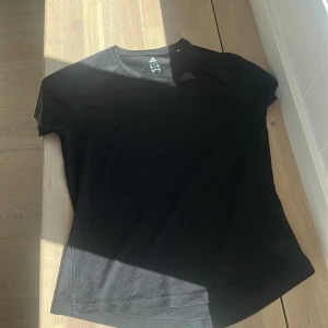 Svart tränings-tshirt från Adidas - Svart kortärmad t-shirt från Adidas med diskret logga på bröstet. Tillverkad i ett lätt och ventilerande polyestermaterial som passar perfekt för träning. Klassisk rund halsringning och sportig passform.