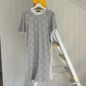 Vit och svart mönstrad klänning Replay - Cool vit och svart klänning från Replay med grafiskt rutmönster framtill och på ärmarna. Baksidan är helvit. Modellen är rak och har korta ärmar och rund hals. Perfekt för dig som gillar statement-plagg med unik design.