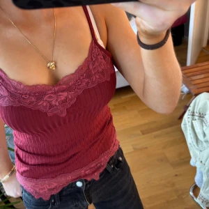 Vinröd ribbad linnetopp med spets - Supersnygg vinröd ribbad linnetopp med tunna axelband och spetsdetaljer i samma färg längs ringningen och nederkanten. Toppen är figurnära i storlek xs!🌹❤️