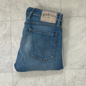 Replay ljusblå jeans straight fit - Säljer ett par ljusblå jeans från Replay med klassisk femficksdesign och snygga slitningar på låret. Jeansen har raka ben och normal passform, med Replay-logga på bakfickan och patch i midjan. Perfekta för en avslappnad stil.